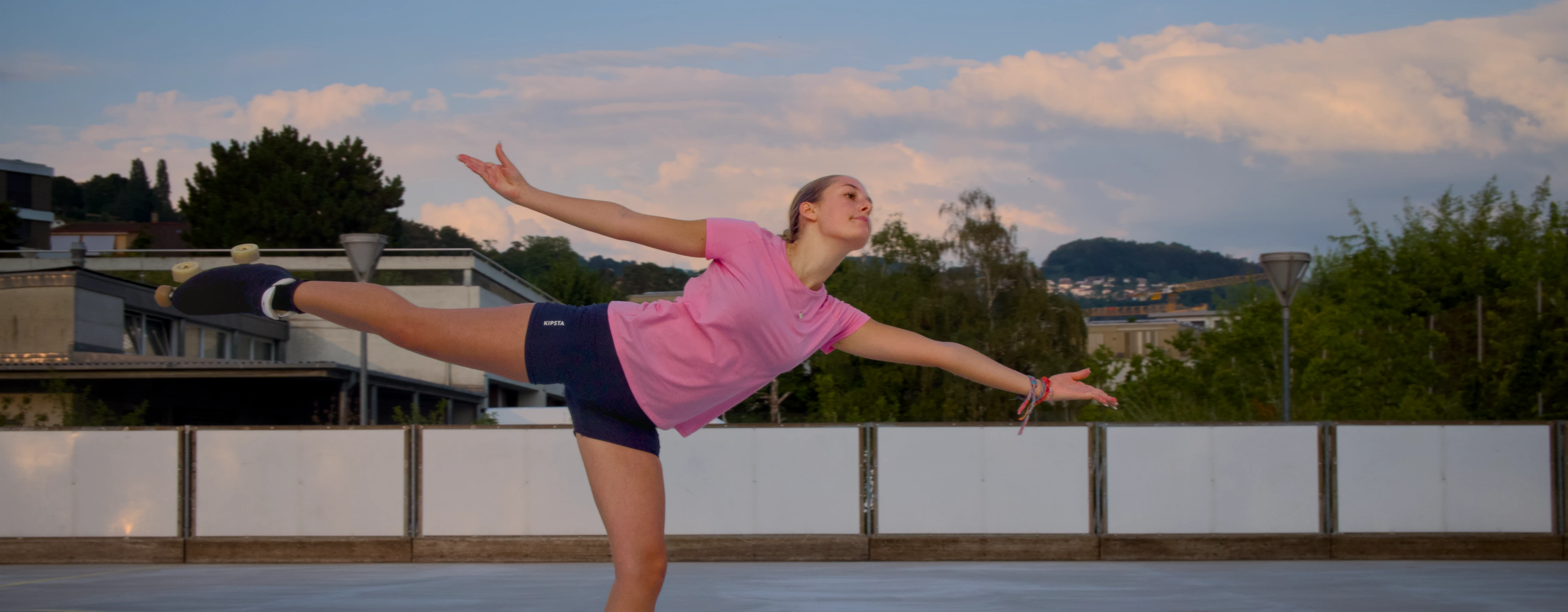 Une patineuse en équilibre arabesque, les bras ouverts sur la piste extérieure